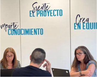 3 personas hablando al lado de un pared con el lema comparte, siente y crea